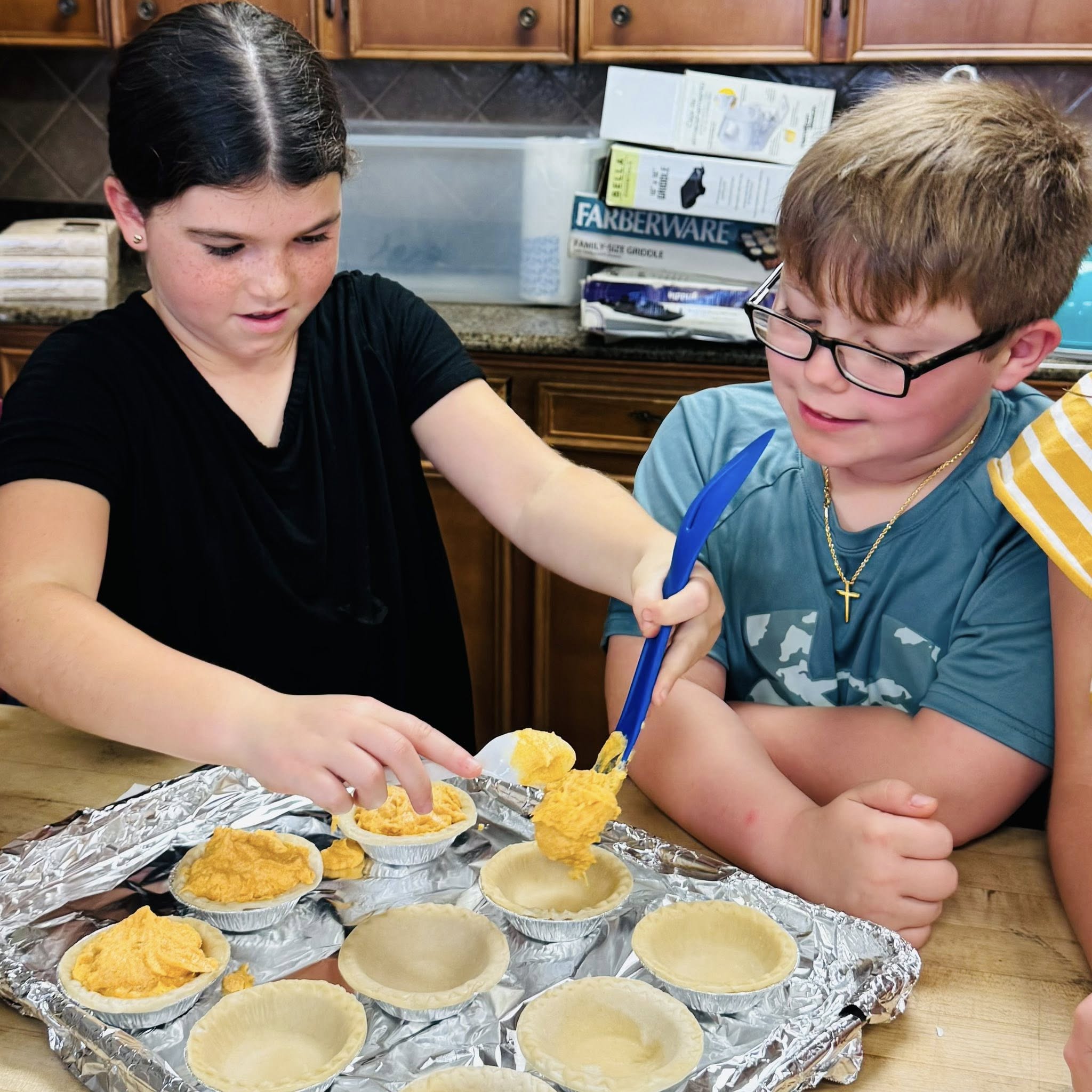A boy watching a girl put pie filling into mini pie shells.